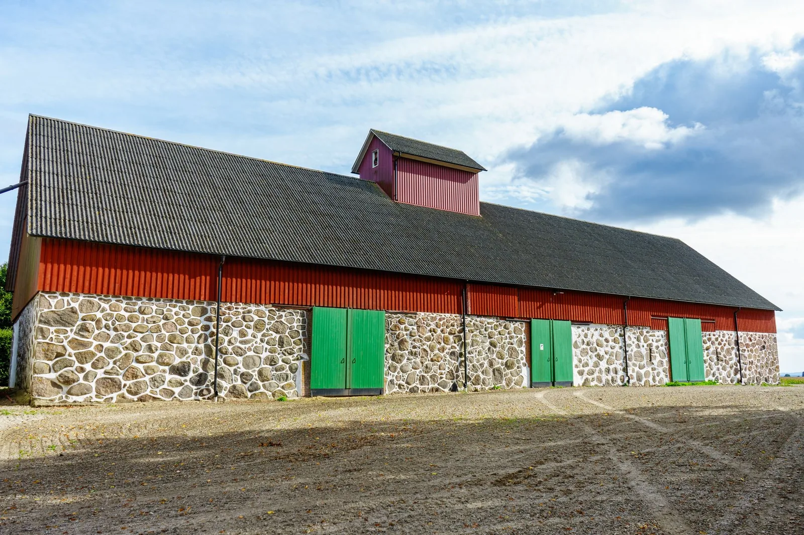 Stone barn with red timber cladding and green doors